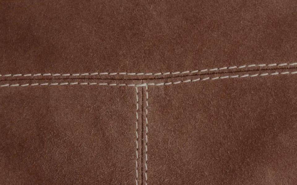 A close view of a tan hide where two panels meet. Two parallel rows of cream thread run either side of the seam, a few millimetres apart, so the join lies flat instead of standing up as a ridge.