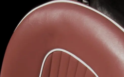 A red vehicle seat whose every seam is outlined by a thin raised white cord sewn into the join. The cord traces the edge of the backrest and the outline of the fluted centre panel, giving the shape a drawn border.
