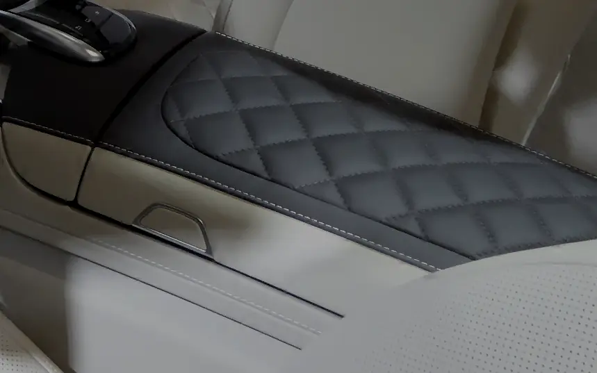 A dark leather armrest quilted into a repeating diamond lattice, each diamond outlined by a machine-stitched line with a raised pad of leather inside it. A pale perforated seat cushion sits alongside for contrast.