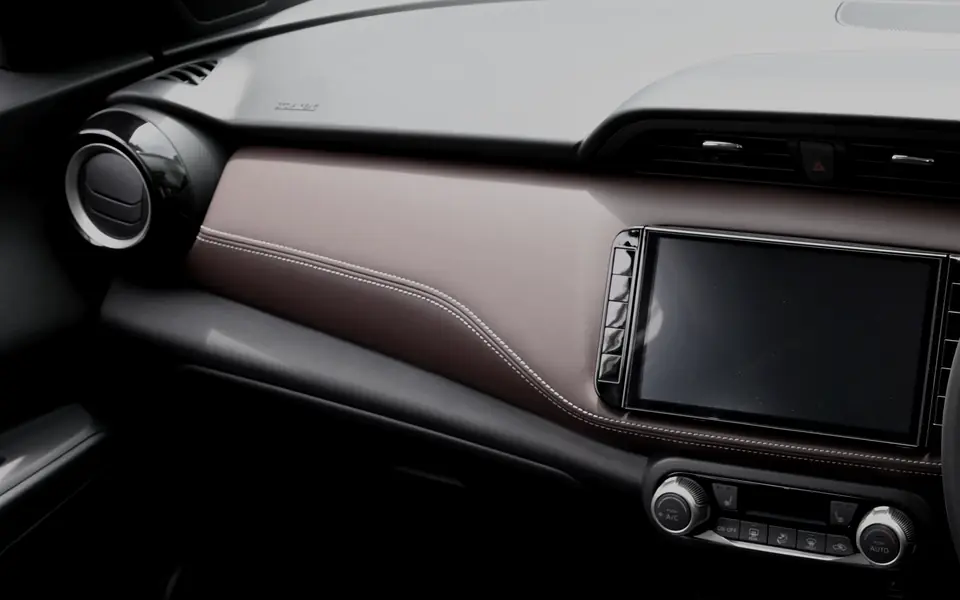 A cabin trimmed in two colours. An oxblood leather panel with a pale stitch line sweeps across the dashboard, meeting a near-black lower panel below it and a pale grey upper panel above, so three tones of the same cabin are visible at once.