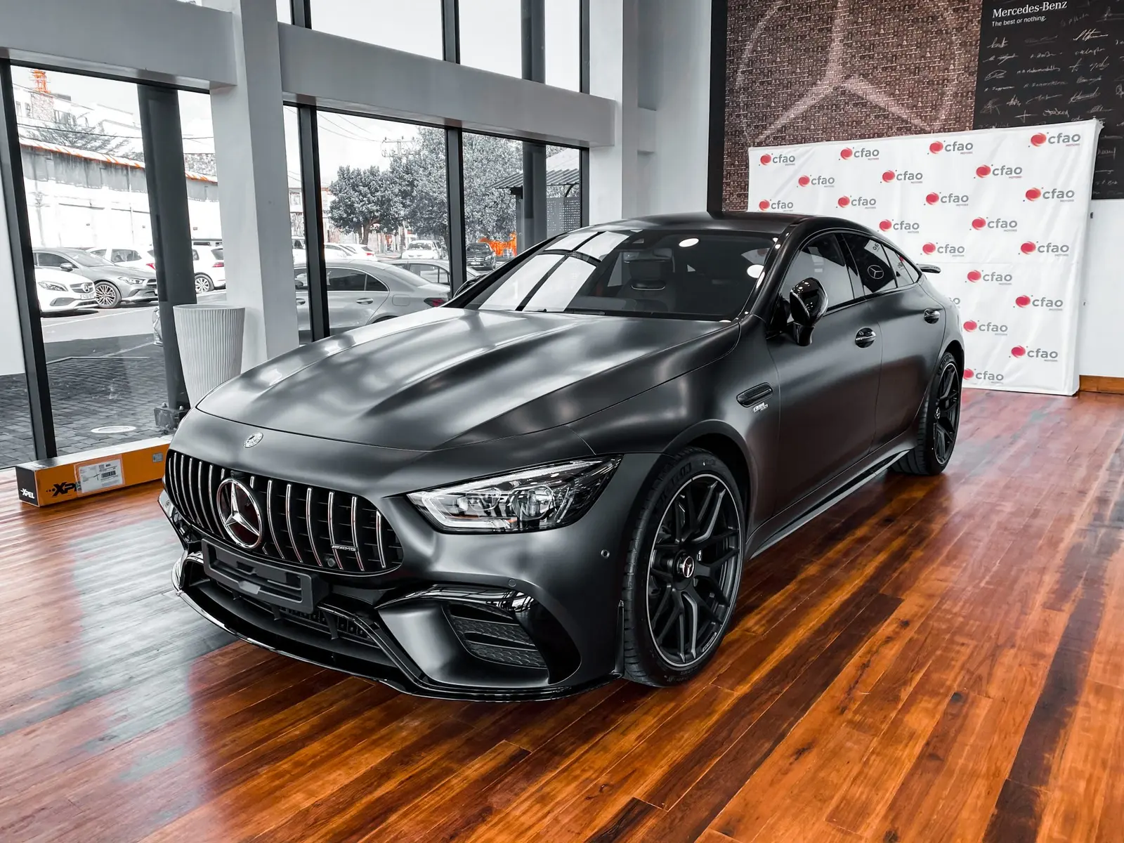 A matte grey Mercedes-AMG GT four-door coupe on a wooden showroom floor