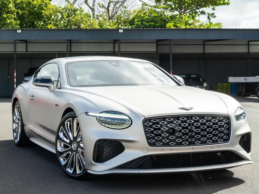 A pale silver Bentley Continental GT photographed three-quarter front outside the workshop