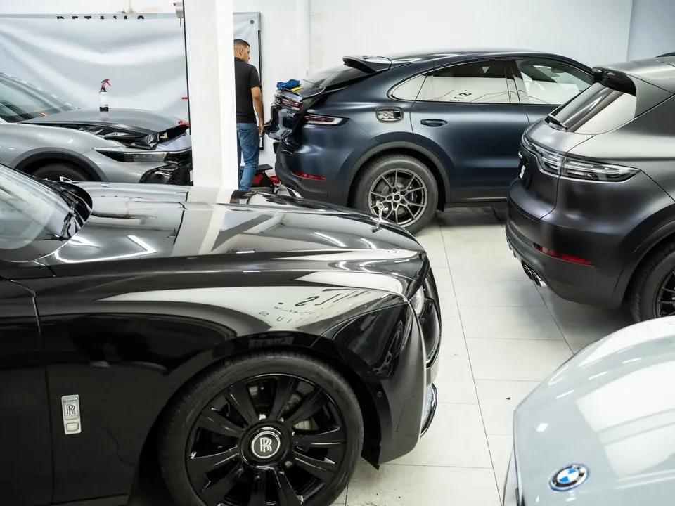 Five cars parked close together inside the workshop, including a black Rolls-Royce, two Porsche Cayennes and a Taycan