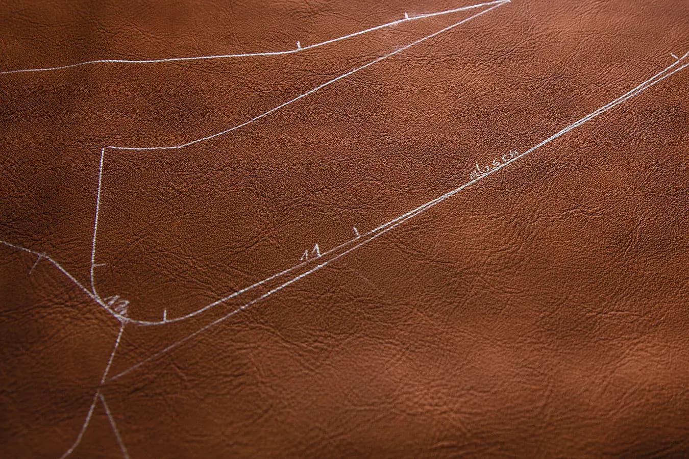 A tan leather hide marked out in white chalk lines ready for cutting